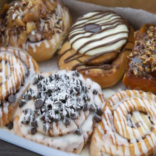 A variety of glazed donuts topped with chocolate, nuts, and fruit, arranged in a box.
