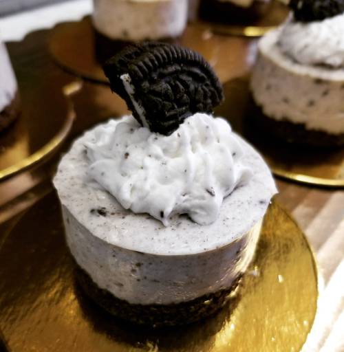 Mini Oreo cheesecake with whipped cream and an Oreo cookie on top, sitting on a gold plate.