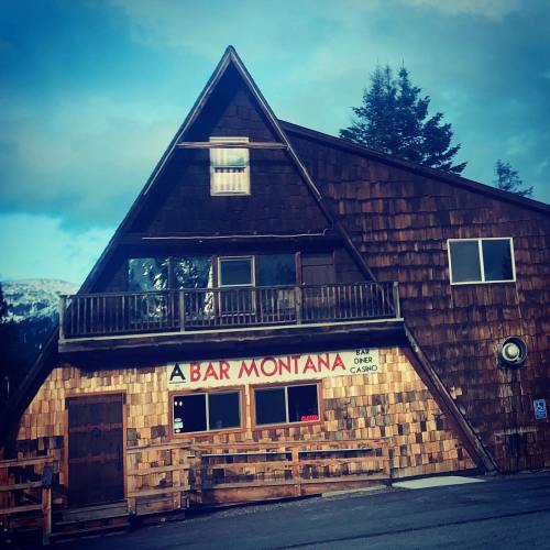 A rustic wooden building with a triangular roof, featuring a sign that reads "A Bar Montana" and a balcony.