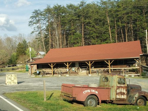 A rustic roadside eatery with a red roof, old truck, and a sign for takeout, surrounded by trees.