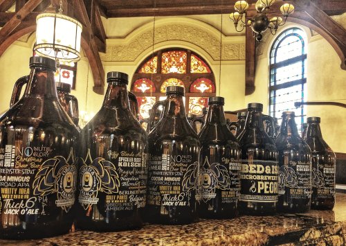 A row of decorative beer growlers on a bar counter, with stained glass windows in the background.