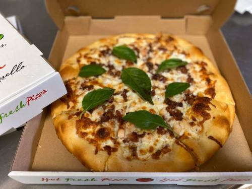 A freshly baked pizza in a box, topped with cheese, meat, and fresh basil leaves.