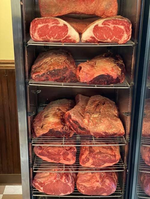 A display case filled with various cuts of raw beef, including ribeyes and briskets, arranged on metal shelves.