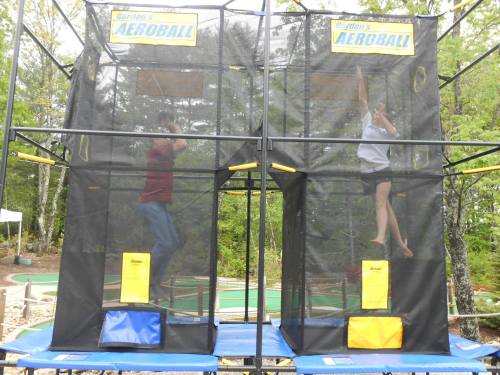 Two people playing Aeroball in enclosed, netted structures surrounded by greenery.