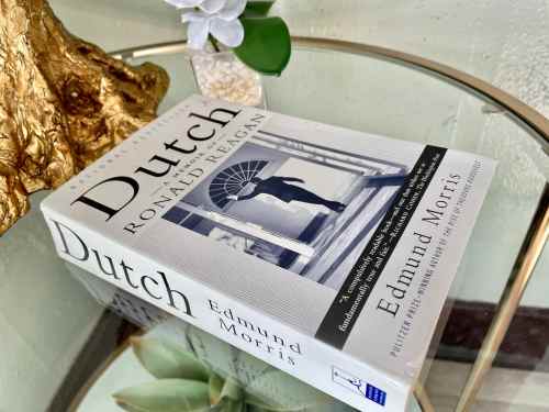 A book titled "Dutch: A Memoir of Ronald Reagan" by Edmund Morris, displayed on a glass table with a decorative plant.
