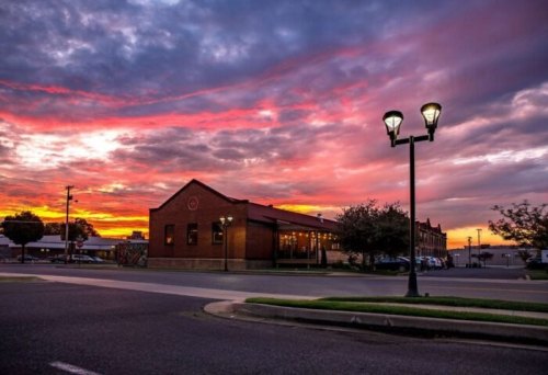 A vibrant sunset casts colorful hues over a brick building and street lamps in a quiet urban setting.
