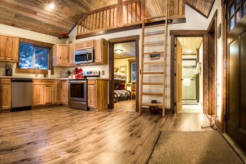 Cozy cabin interior featuring a kitchen, wooden accents, a staircase, and a view of a bedroom and bathroom.