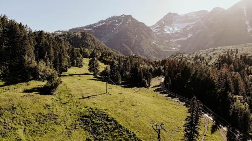 A scenic view of green hills and mountains under a clear sky, with a winding road and ski lift in the foreground.