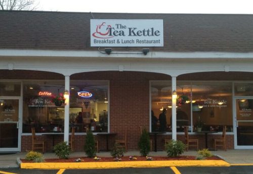 Exterior view of The Tea Kettle restaurant, featuring a sign, open windows, and a welcoming entrance.