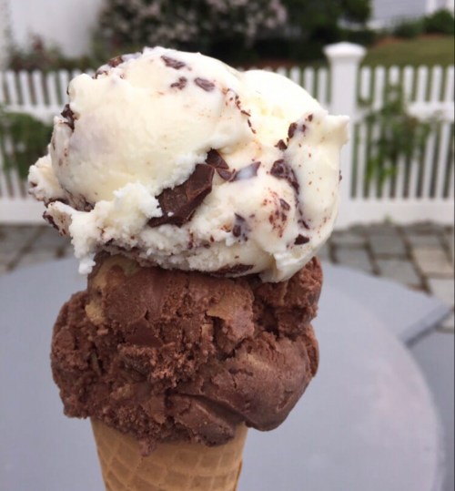A close-up of a two-scoop ice cream cone with chocolate and vanilla flavors, topped with chocolate shavings.