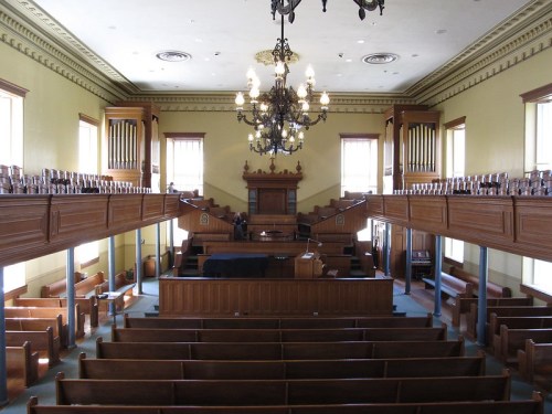 Interior of a historic courtroom featuring wooden benches, a judge's bench, and a chandelier.