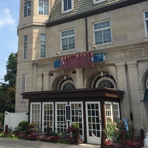 Exterior of a building with a sign reading "The Greenhouse Lodge," featuring large windows and colorful flower beds.
