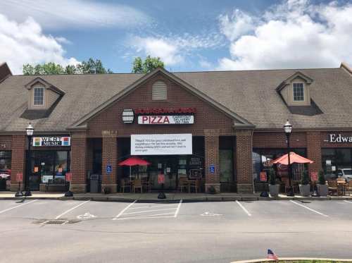 Exterior of Bourbon House Pizza with outdoor seating, a sign thanking customers, and a clear blue sky.