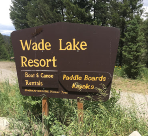 Sign for Wade Lake Resort, listing boat, canoe, paddle board, and kayak rentals amidst greenery and trees.