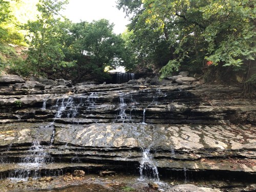 A serene waterfall cascading over layered rocks, surrounded by lush green trees in a peaceful natural setting.