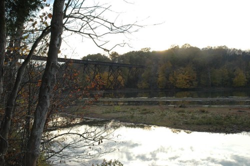 A tranquil scene of a river with a bridge in the background, surrounded by trees and autumn foliage.