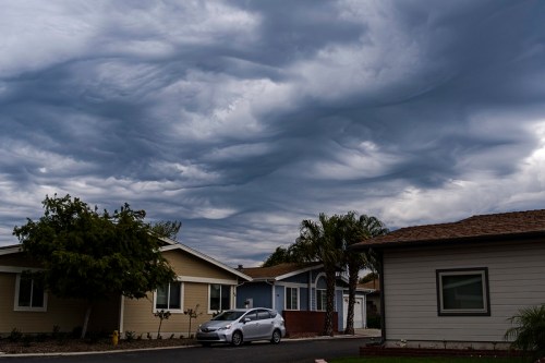A cloudy sky with swirling gray clouds above a residential neighborhood and parked car.