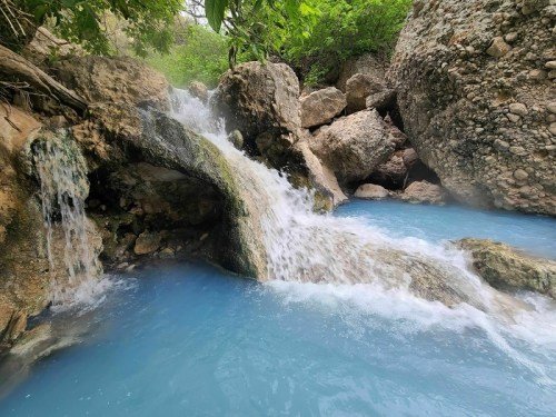 A serene waterfall cascades over rocks into a turquoise pool, surrounded by lush greenery.