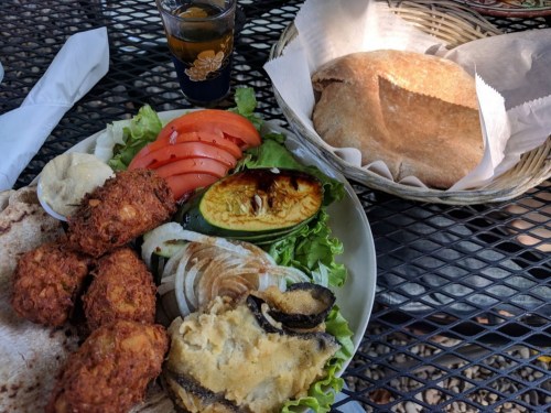 A plate of falafel, fresh vegetables, and hummus, with a side of pita bread and a small glass of drink.