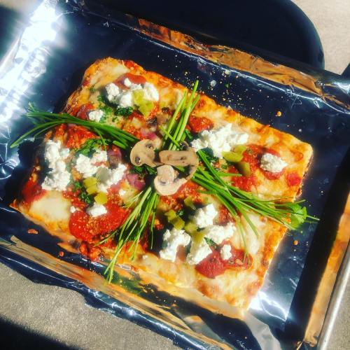 A rectangular pizza topped with tomato sauce, cheese, mushrooms, green peppers, and fresh herbs on a foil-lined tray.
