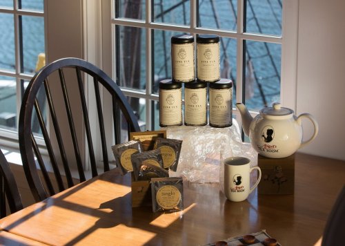 A cozy tea setup featuring jars of tea, a teapot, and tea bags on a wooden table by a window with a water view.