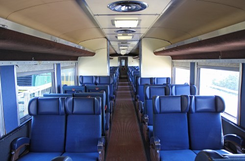Interior of a train carriage featuring rows of blue upholstered seats and large windows.
