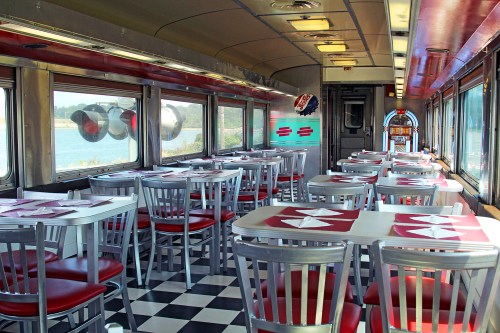 Interior of a retro diner with red and white decor, checkered floor, and large windows overlooking a scenic view.