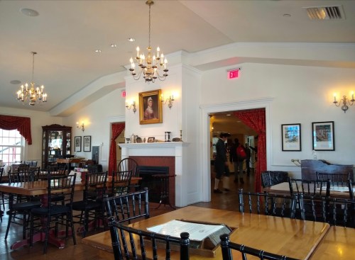 Interior of a restaurant with wooden tables, chandeliers, and framed artwork, featuring a warm, inviting atmosphere.