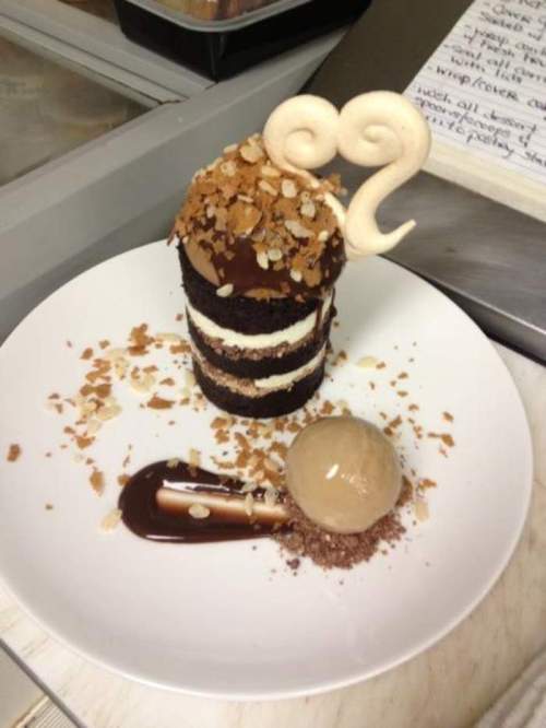A layered chocolate dessert topped with crunchy flakes, a swirl decoration, and a scoop of coffee ice cream on the side.