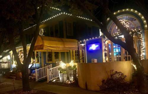 A cozy restaurant at night, adorned with festive lights and decorations, surrounded by trees.