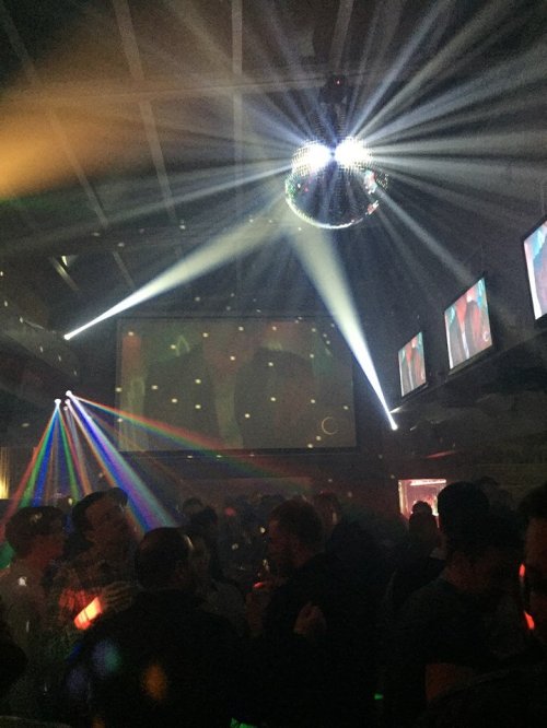 A lively nightclub scene with colorful lights, a disco ball, and people dancing under vibrant beams.