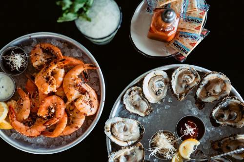 A seafood platter featuring shrimp and oysters on ice, with lemon wedges and dipping sauces.