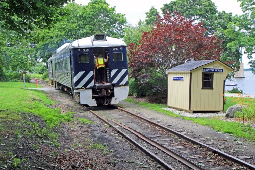 A vintage train on tracks near a small building labeled "Bristol Ferry," surrounded by greenery and trees.