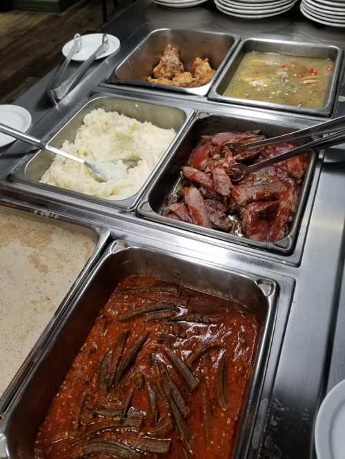A buffet spread featuring fried chicken, mashed potatoes, meat in sauce, and okra in a rich tomato sauce.