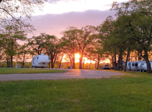 A serene sunset behind trees at a campground, with RVs parked along a winding road.