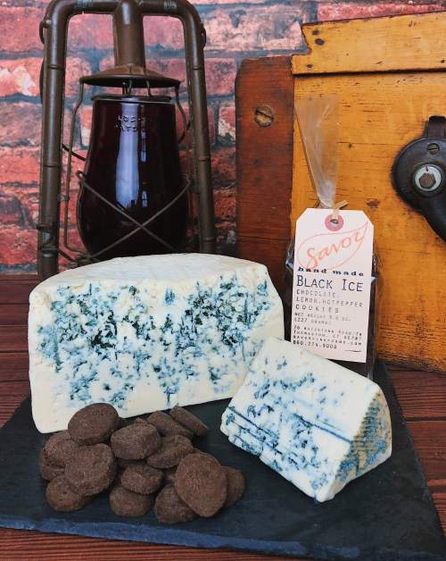 A slate platter with blue cheese, chocolate discs, and a bottle labeled "Black Ice" on a rustic background.