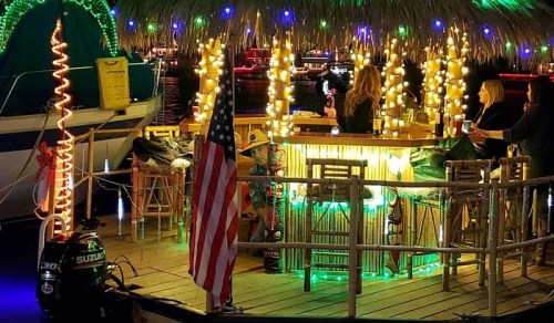 A vibrant tiki bar with colorful lights, surrounded by boats and an American flag in the foreground.