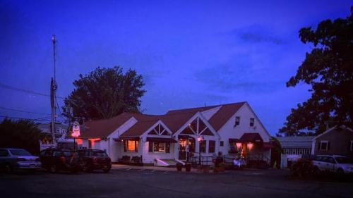 A cozy restaurant at dusk, with warm lights glowing from the windows and parked cars in the foreground.