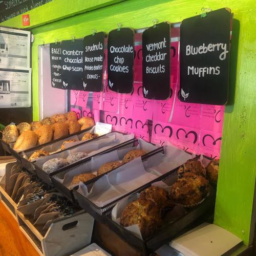 A display of baked goods including muffins, biscuits, and cookies, with menu signs on a vibrant green wall.