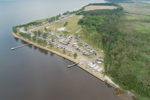 Aerial view of a lakeside campground with RVs, docks, and green trees along the shoreline.
