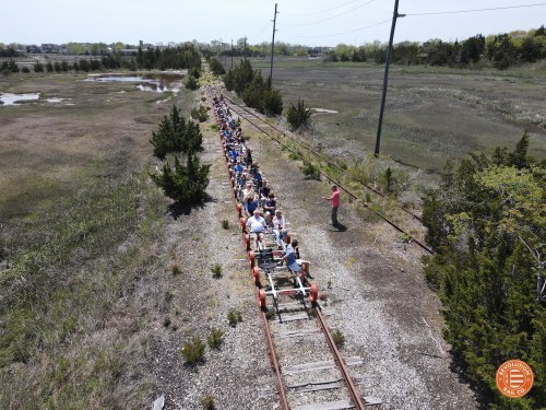 A large group of people riding on a rail bike along an old railway track through a grassy landscape.