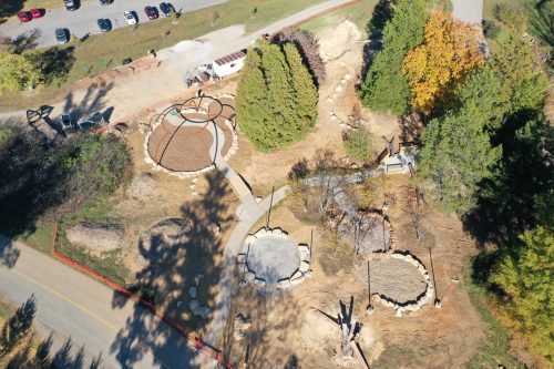 Aerial view of a park under construction, featuring pathways, circular areas, and surrounding trees.