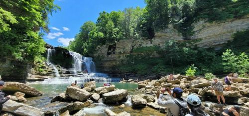 A scenic waterfall surrounded by lush greenery, with people exploring the rocky area and enjoying the view.