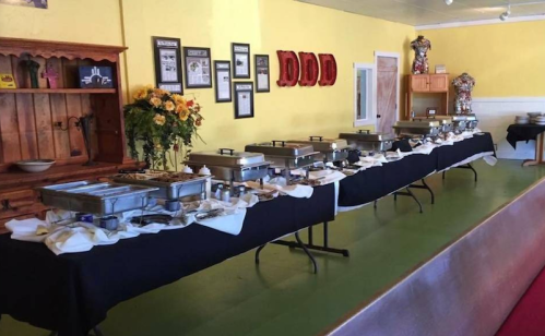 A buffet setup with multiple chafing dishes on tables, decorated with flowers and framed pictures on the wall.