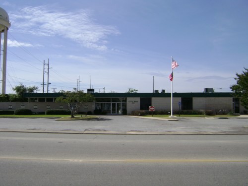 A low-rise building with a flagpole and water tower in the background, set along a quiet street.