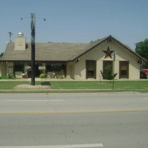 A single-story building with a thatched roof, decorative star, and landscaped front yard along a road.