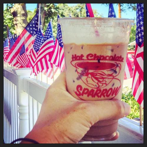 A hand holding a cup of iced hot chocolate in front of numerous small American flags.