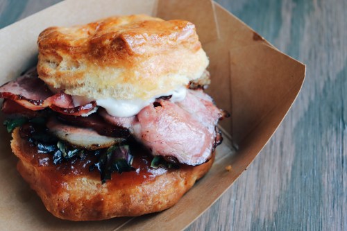 A delicious sandwich featuring layers of meat, greens, and sauce, all nestled in a flaky biscuit.