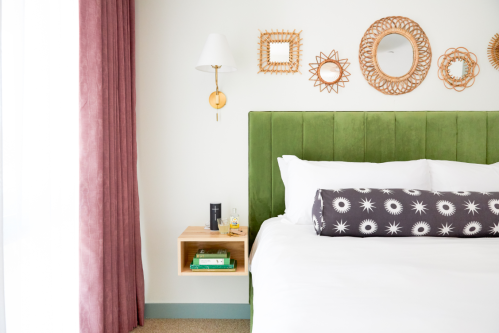 A cozy bedroom featuring a green upholstered headboard, decorative mirrors, and a bedside table with books and decor.