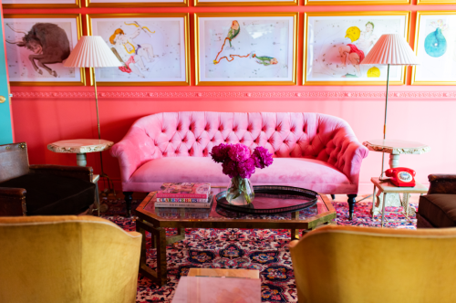 A vibrant living room featuring a pink tufted sofa, colorful artwork, and a floral centerpiece on a coffee table.